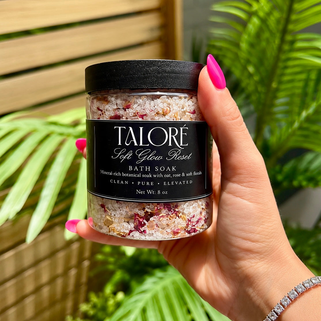 Hand holding a jar of Talore bath soak with plants in the background