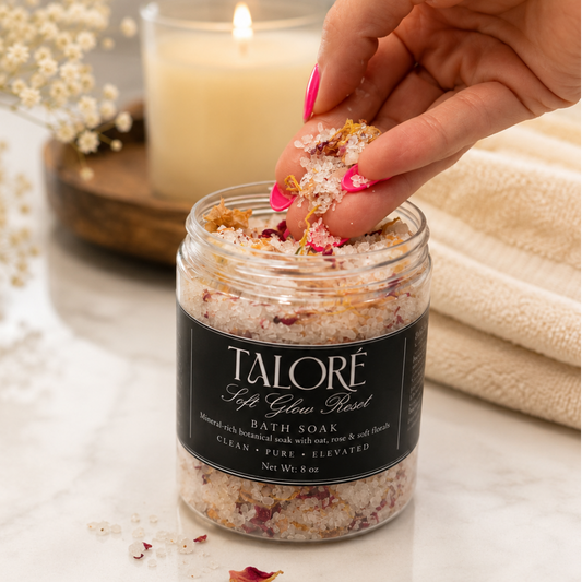 Person using a jar of Talore bath soak with a candle and flowers in the background